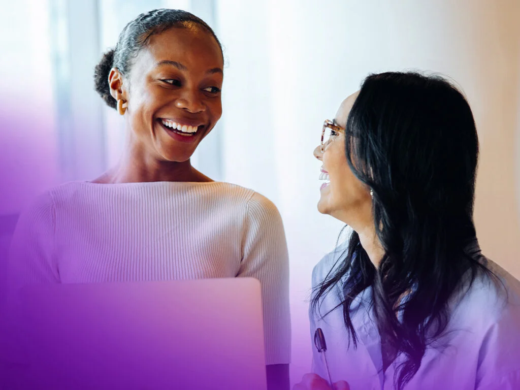 two women talking and working on a laptop